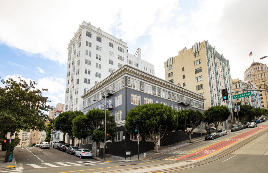 A street view of a city with a white building on the left and a grey building on the right.